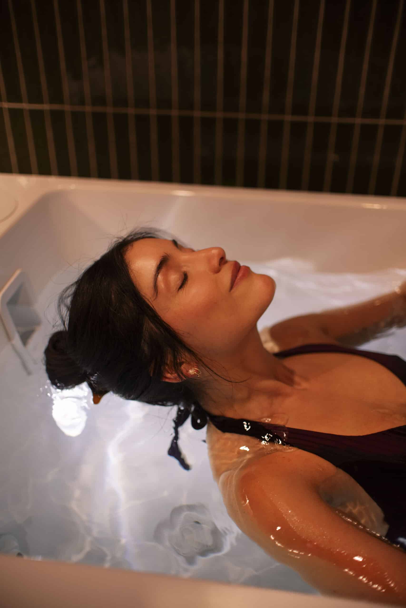 Woman relaxing in a warm soak, eyes closed, post-recovery calm